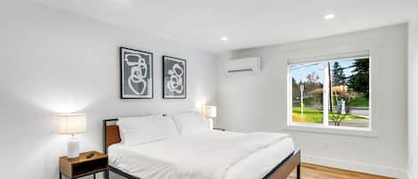 A modern bedroom with a wooden floor, a bed with white bedding, two bedside lamps, and two abstract wall art pieces.