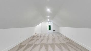 Une pièce mansardée spacieuse, avec un plafond haut, des murs blancs et un tapis à motifs.