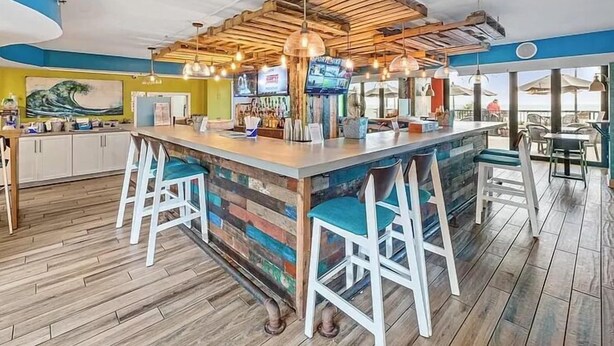 Angolo bar con soffitto in legno, sgabelli da bar e schermo televisivo.