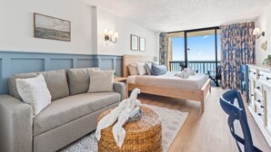 Una camera da letto con un letto, un divano, un tavolino in vimini e vista sull'oceano.