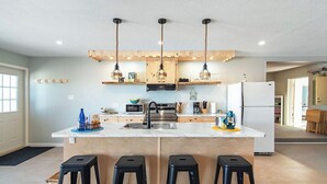 A modern kitchen with a central island, bar stools, hanging pendant lights, and wooden cabinetry. - Oceanfront Central Seawalk Location | Patio, BBQ (Campbell River)