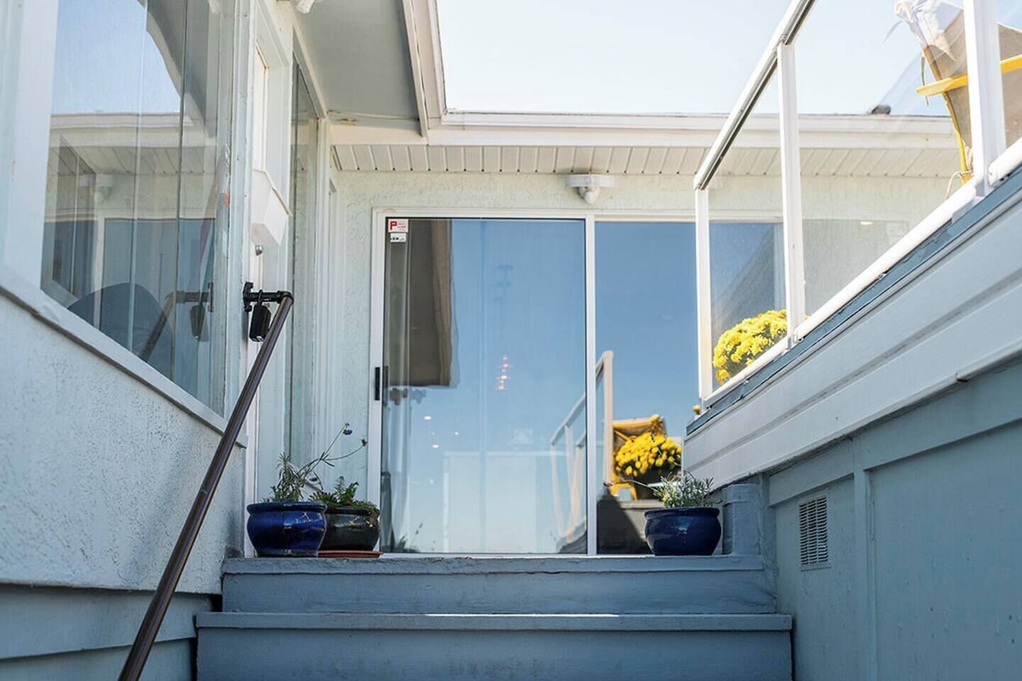 A residential entryway with a glass door, potted plants, and a clear view of the sky.