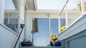 A residential entryway with a glass door, potted plants, and a clear view of the sky. - Oceanfront Central Seawalk Location | Patio, BBQ (Campbell River)