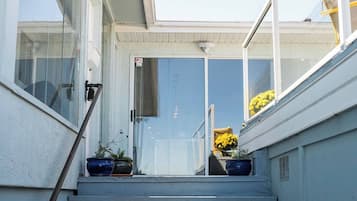 A residential entryway with a glass door, potted plants, and a clear view of the sky.