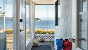 A balcony with a view of the ocean, a door, and a small entryway with a mat and potted plants. - Oceanfront Central Seawalk Location | Patio, BBQ (Campbell River)