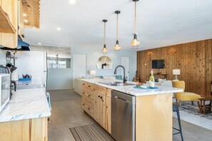 A modern kitchen with wooden cabinets, a built-in dishwasher, and pendant lighting.