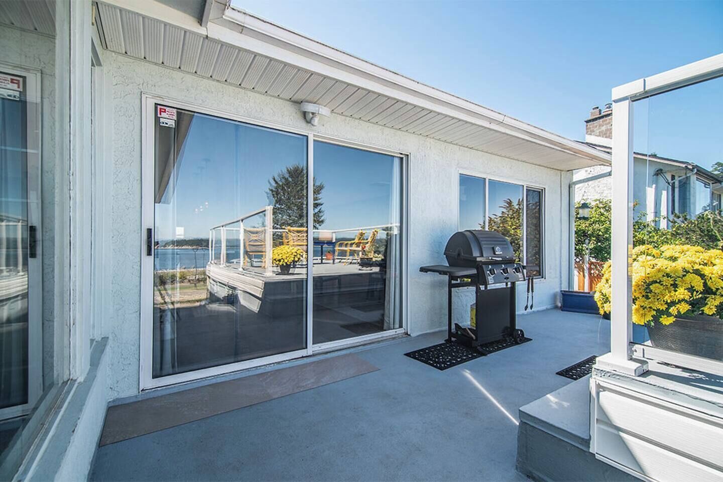 A covered patio with a grill, sliding glass doors, and a view of the water.