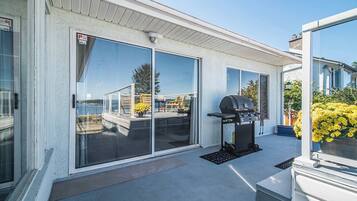 A covered patio with a grill, sliding glass doors, and a view of the water.