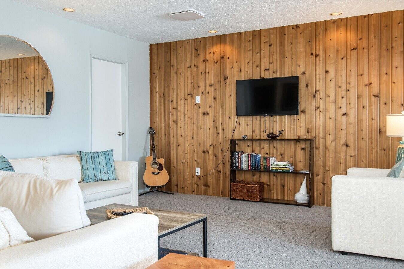 Una sala de estar moderna con una pared de paneles de madera, un televisor de pantalla plana, una guitarra y una estantería.