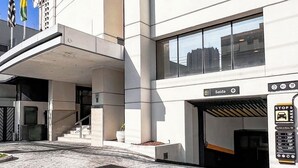 A modern building with a prominent entrance, a sign indicating a parking area, and multiple flags on the roof. - Suite Luxo a 5min do aerop de Congonhas (São Paulo)