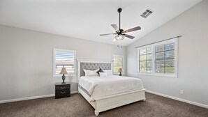 A bedroom with a large bed, two bedside tables, a ceiling fan, and two windows with blinds. - Stay with the Shay’s (Phoenix)