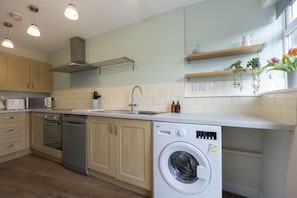 Una cocina moderna con armarios de madera, lavavajillas integrado, lavadora e iluminación colgante.