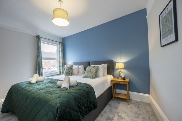 A bedroom with a large bed, a nightstand, a lamp, and a framed picture on the wall.