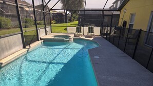 Una piscina con un recinto in vetro, circondata da una zona patio con sedie e un tubo da giardino.