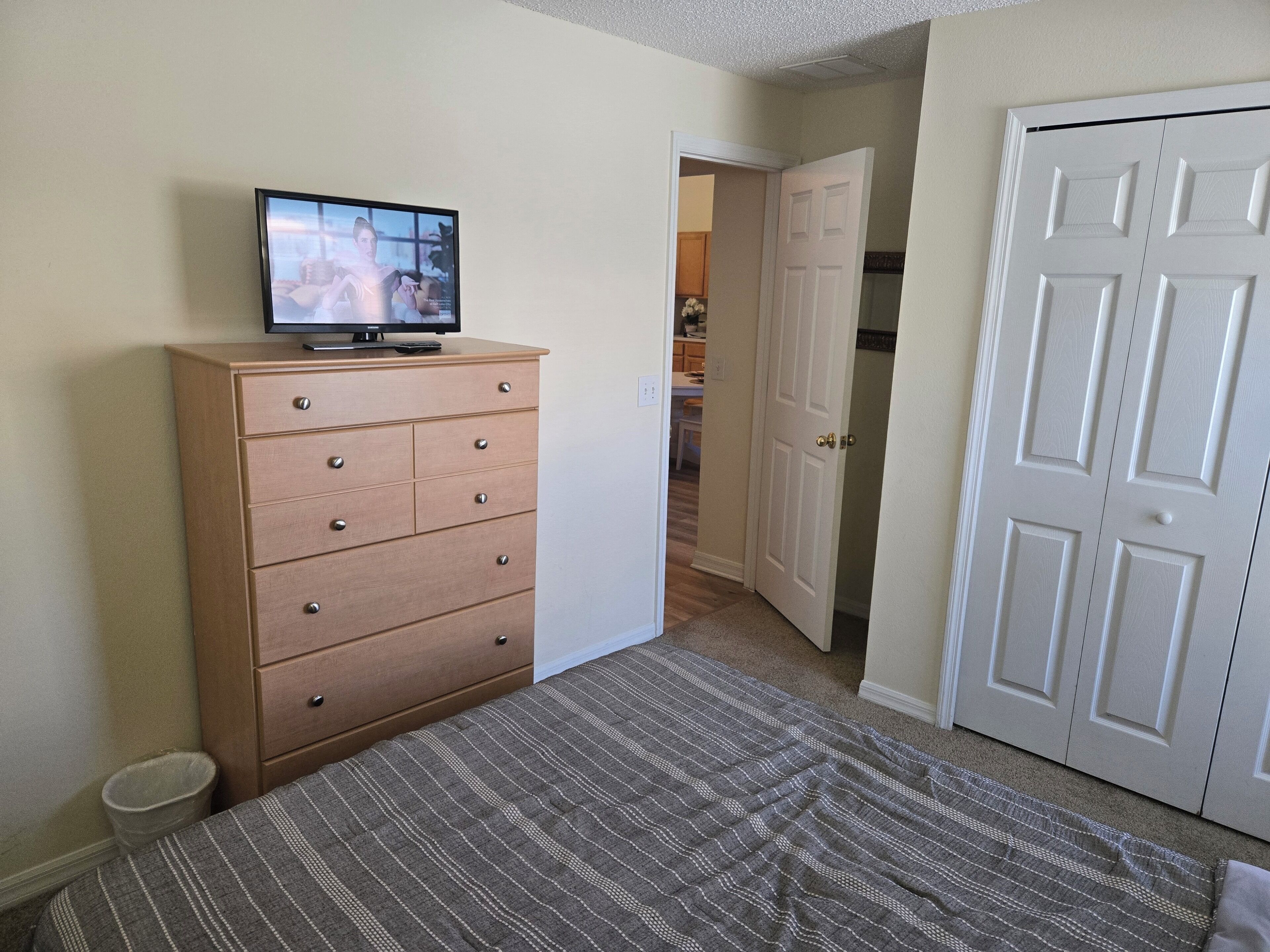 A bedroom with a bed, a dresser, a television on the dresser, and a door leading to another room.