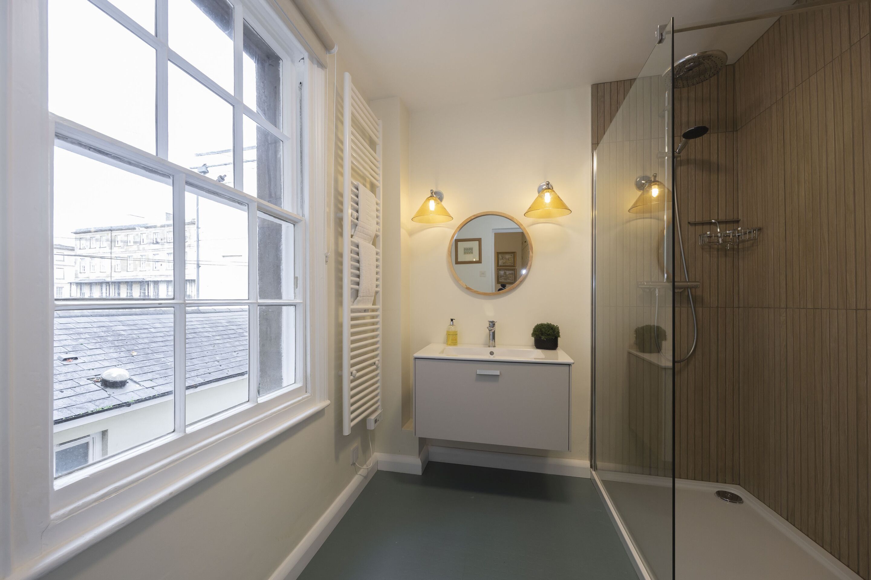 A bathroom with a window, a sink with a mirror, and a shower.
