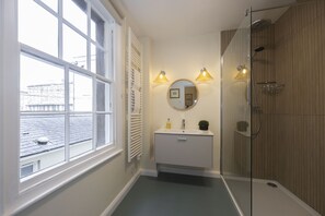 Ein Badezimmer mit Fenster, Waschbecken mit Spiegel und Dusche.
