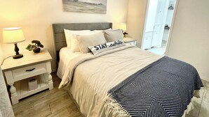 Een slaapkamer met een bed, nachtkastjes, een lamp, een kleine plant, een schilderij en een inloopkast.