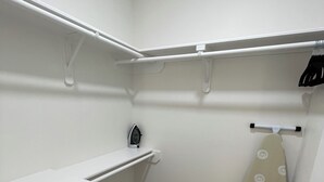 Een compacte, overzichtelijke kast met witte opbergunits, een kledingroede en een klein strijkplank.