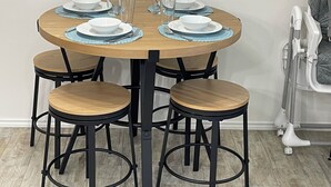 Een ronde eettafel met vier stoelen, elk met een houten zitvlak en zwart metalen frame. De tafel is gedekt met witte borden, kommen en glazen.
