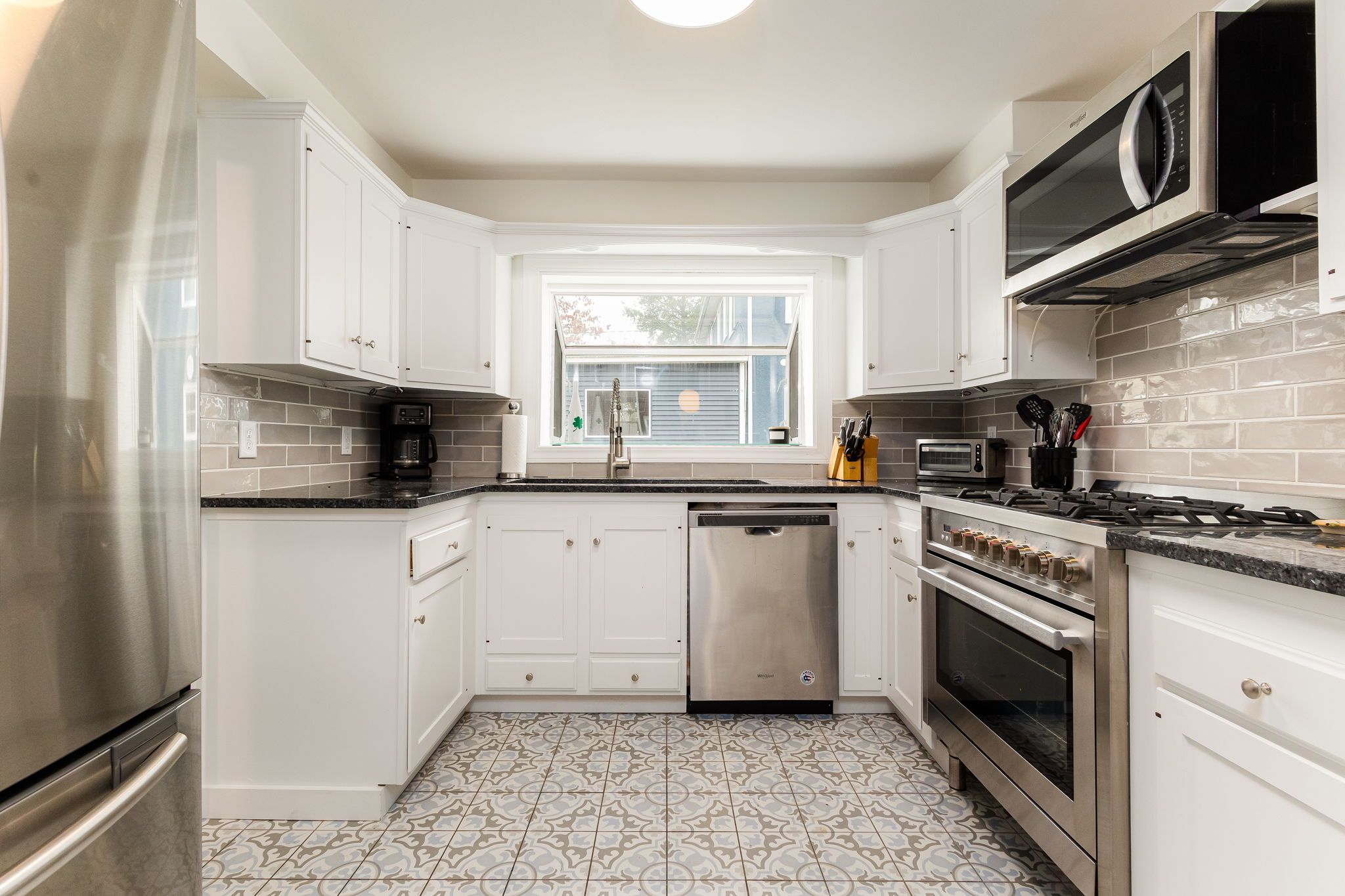A modern kitchen with white cabinets, stainless steel appliances, and patterned tile flooring.