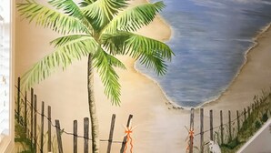 Une fresque représentant une scène de plage avec un palmier, une clôture en bois et une décoration en forme d’étoile de mer sur un escalier.