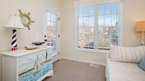Une chambre avec une commode sur le thème de la marine, une fenêtre avec des stores et un lit agrémenté d’un coussin à rayures.