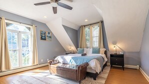 Une chambre à coucher comprenant un lit, un banc, une table de chevet, un ventilateur de plafond et de grandes fenêtres.