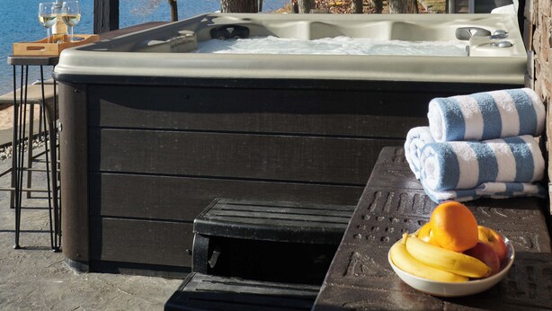 Een hottub met een houten terras, een tafel met handdoeken en een schaal fruit.