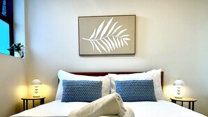 Una cama bien hecha con una almohada de estampado azul, una toalla blanca y un cuadro con una hoja sobre ella.