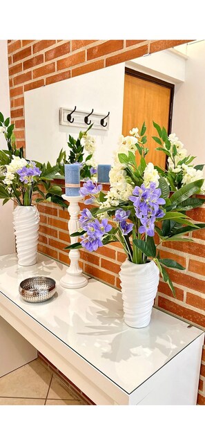 Ein Empfangsbereich mit einer weißen Theke, zwei weißen Vasen mit Blumen, einem Kerzenständer und einer kleinen Metallschale.