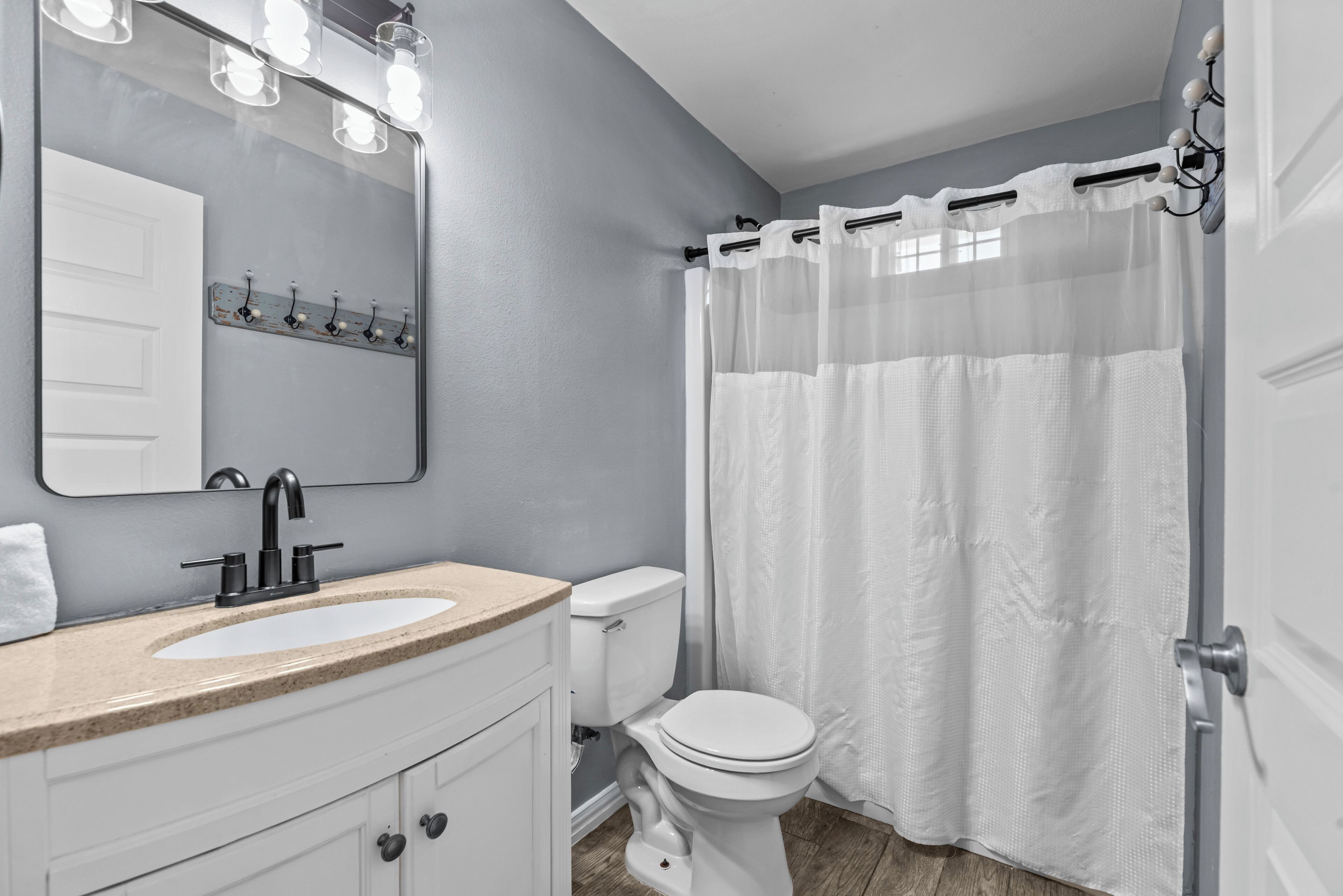A bathroom with a white sink, a mirror with lights, a toilet, and a shower curtain.