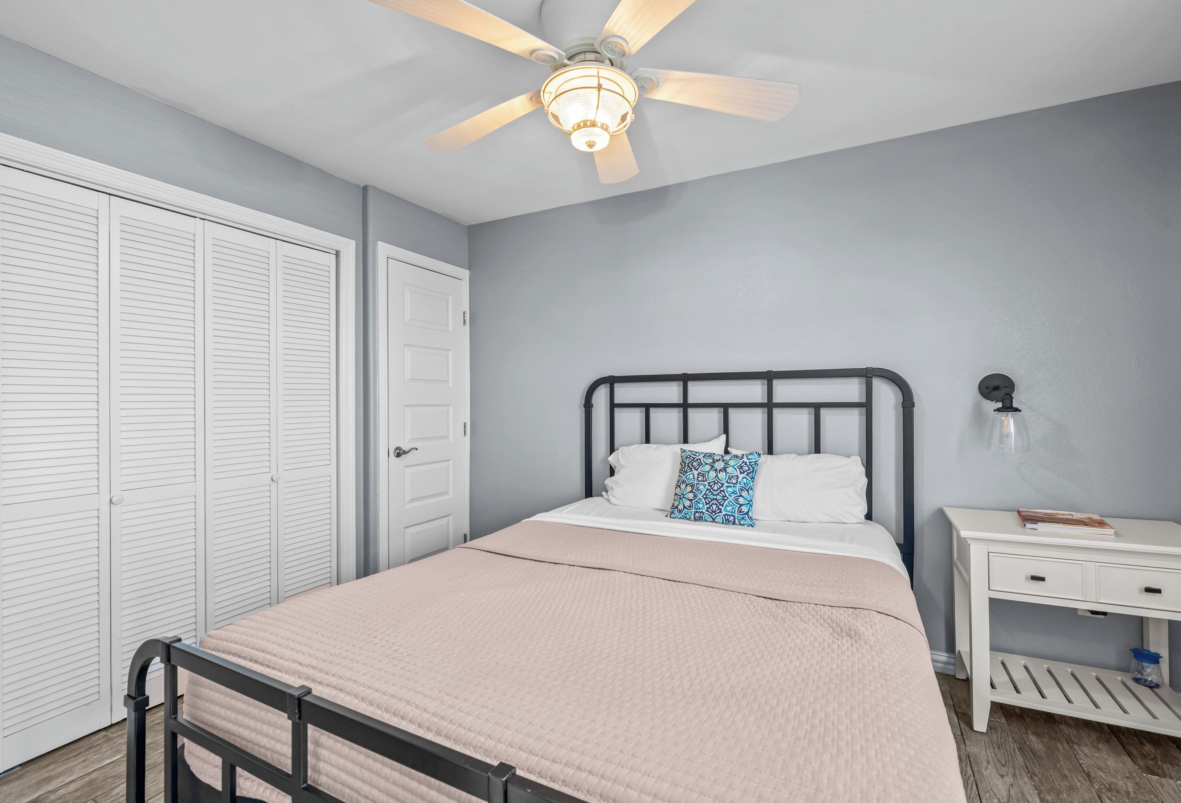 A bedroom with a bed, a nightstand, a ceiling fan, and a wardrobe.