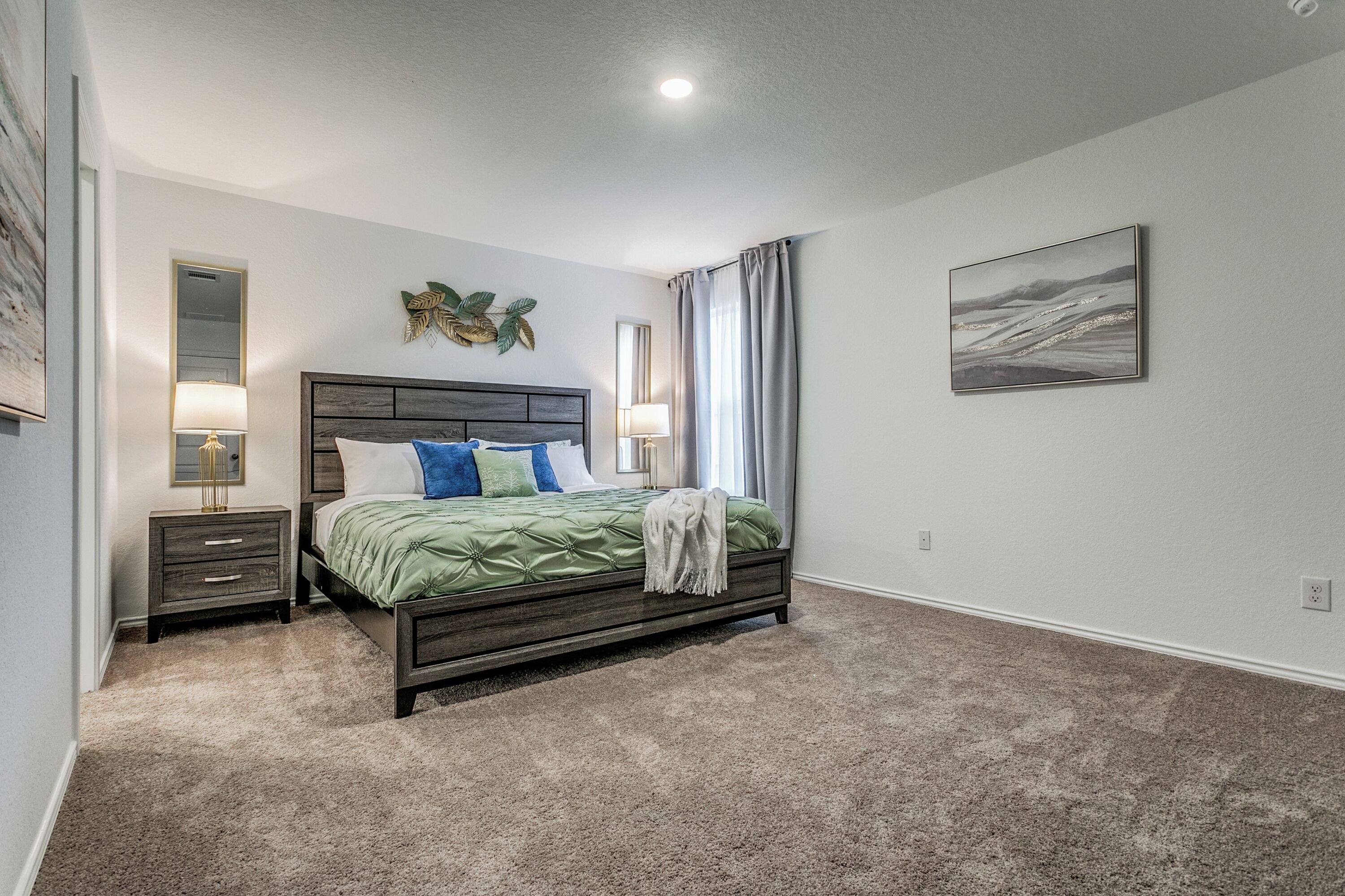 A bedroom with a bed, nightstands, a mirror, and a painting on the wall.