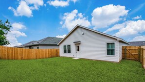 Une maison de plain-pied à l’extérieur blanc, avec une porte d’entrée et un petit jardin devant, délimité par une clôture en bois.