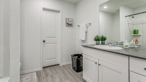 Une salle de bain avec une porte blanche, un lavabo, un miroir et une poubelle.