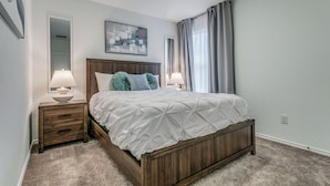 Une chambre à coucher avec un lit en bois, deux tables de chevet avec des lampes, un grand miroir et un tableau au mur.