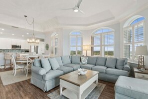 Ein geräumiges Wohnzimmer mit einer Eckcouch, einem Holztisch und einem Essbereich mit weißen Schränken und einer Chandelüster.