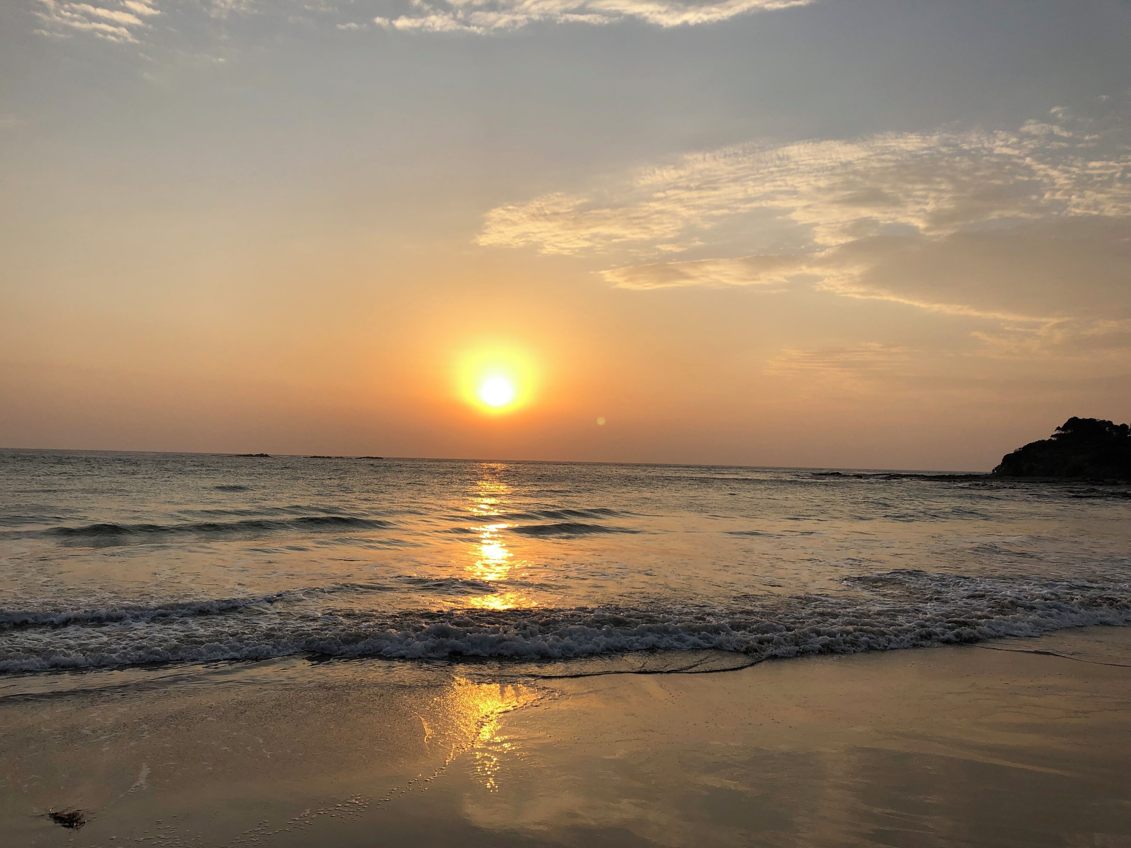 A beach at sunset with the sun reflecting on the water.