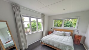 A bedroom with a bed, two bedside tables, a mirror, and two windows. - Sunny 3-bedroom home in Nelson, family friendly with large fenced garden (Nelson)