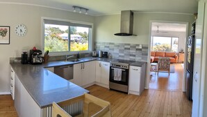 A modern kitchen with a central island, stainless steel appliances, and a view to a living area. - Sunny 3-bedroom home in Nelson, family friendly with large fenced garden (Nelson)