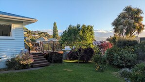 A house with a deck, a small garden with various plants, and a clear sky. - Sunny 3-bedroom home in Nelson, family friendly with large fenced garden (Nelson)
