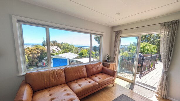 A spacious living room with a leather sofa, large windows, and a view of the outdoors. - Sunny 3-bedroom home in Nelson, family friendly with large fenced garden (Nelson)