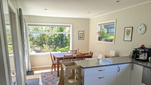 A modern kitchen with white cabinets, a wooden dining table, and a coffee machine. - Sunny 3-bedroom home in Nelson, family friendly with large fenced garden (Nelson)