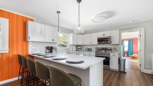 Una cocina moderna con armarios blancos, una isla grande con taburetes de bar y vista a un comedor.