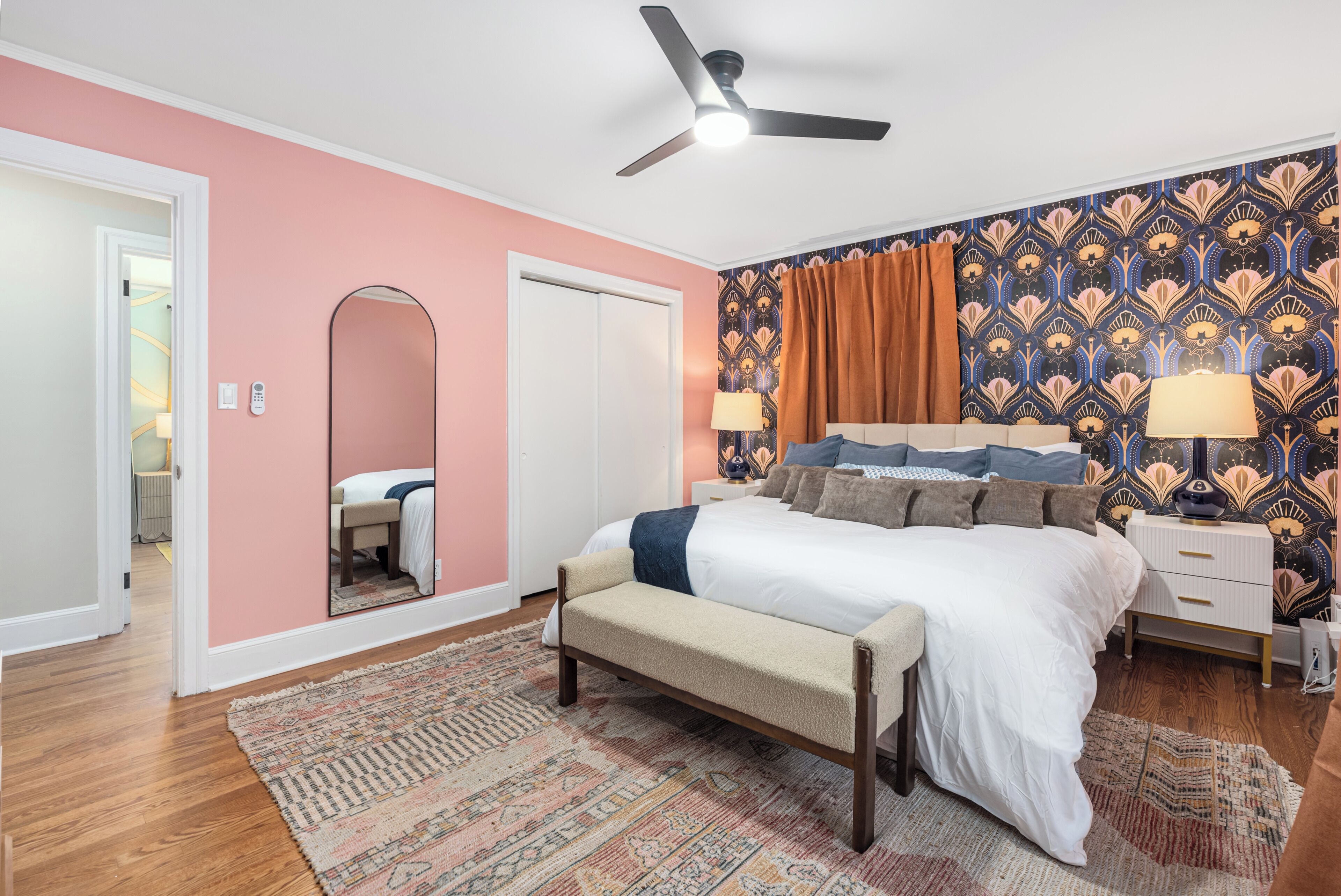 A bedroom with a bed, bench, bedside tables, a ceiling fan, and a patterned wall.