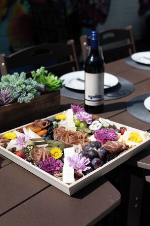 Uma tábua de madeira com queijos variados, frutas e flores sobre uma mesa.