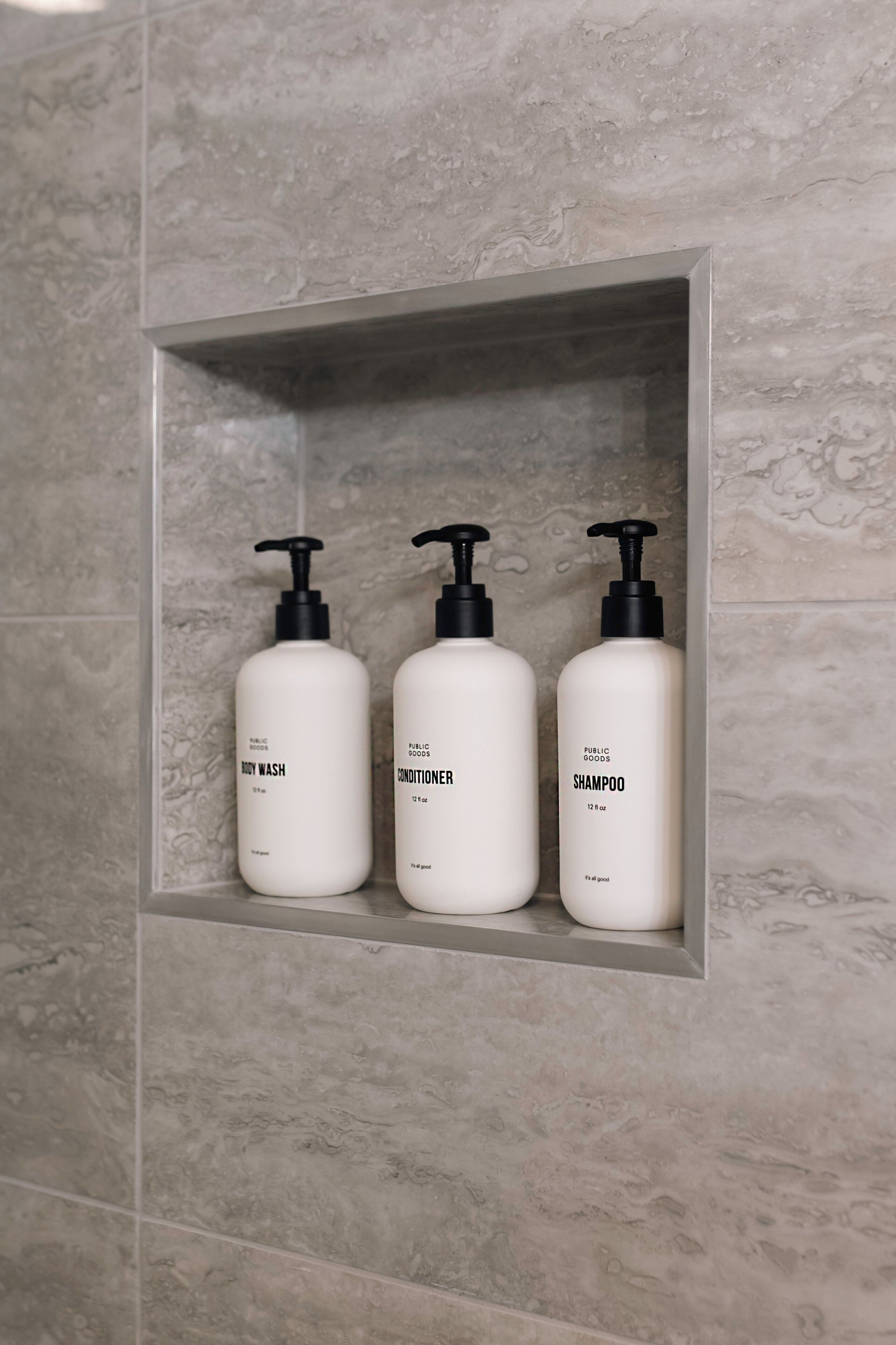 A bathroom shelf with three white bottles labeled 'BODY WASH,' 'CONDITIONER,' and 'SHAMPOO.'