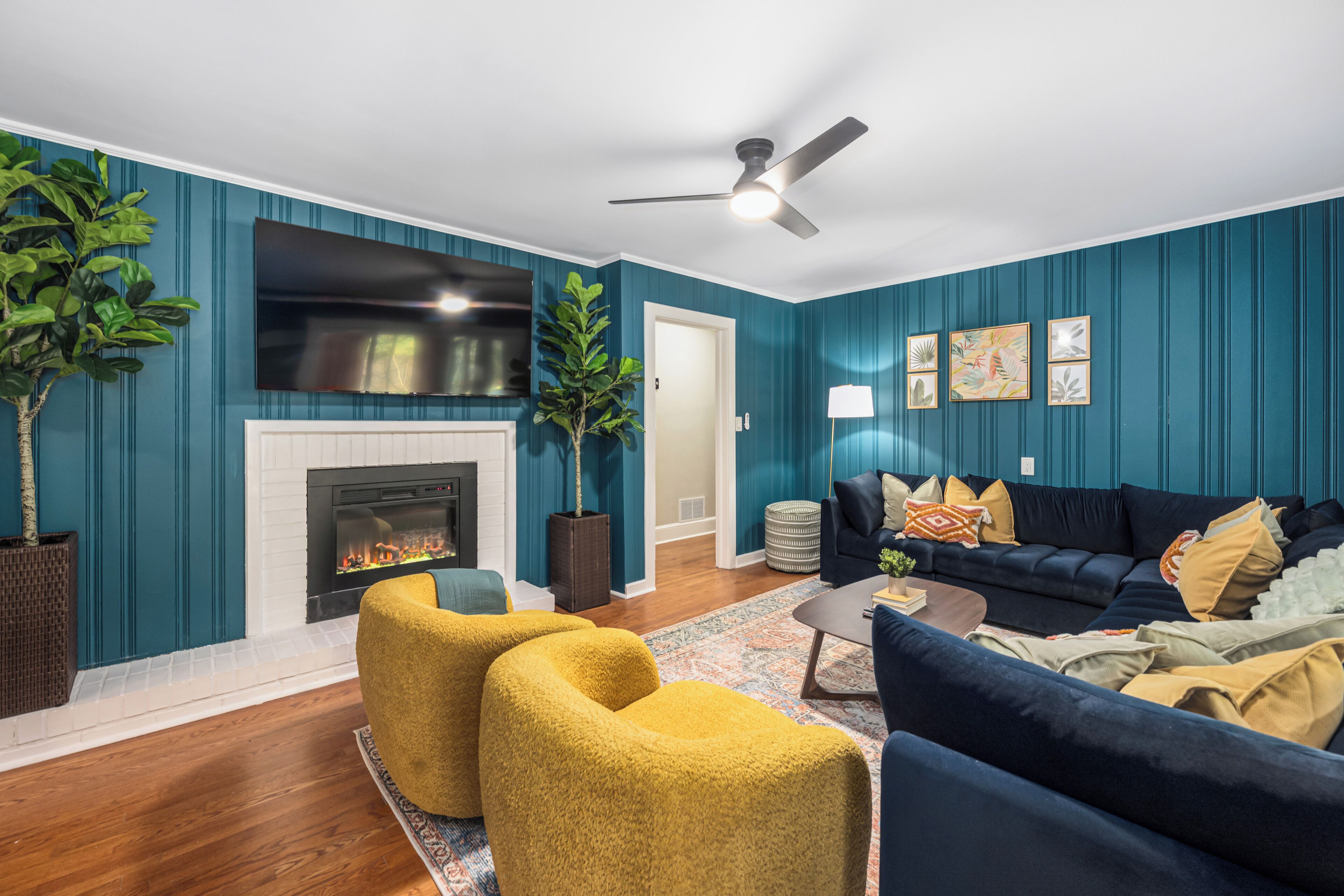 A living room with teal walls, a fireplace, a ceiling fan, and a dark blue sofa with yellow cushions.