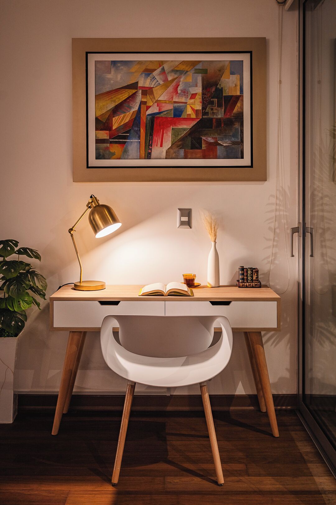 A modern desk with a lamp, a book, and a vase with dried plants.